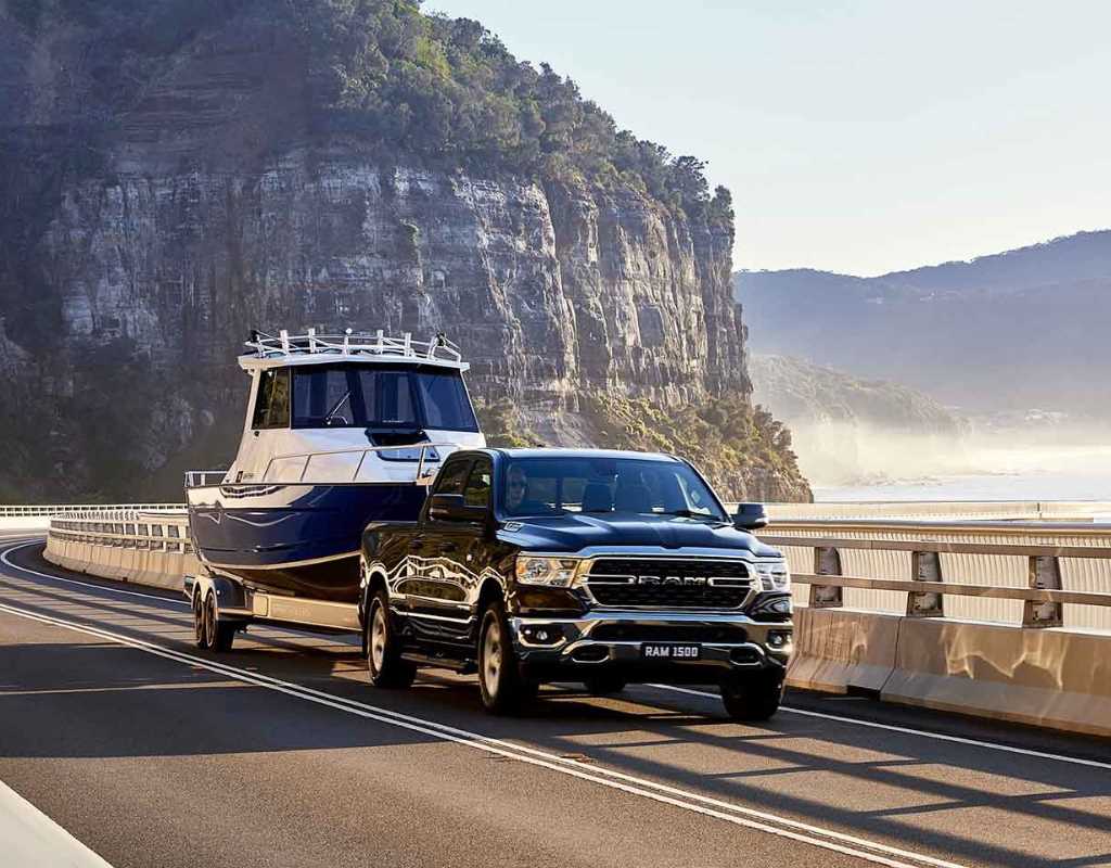 A RAM truck towing a boat on a highway for a Village Motors marketing campaign.